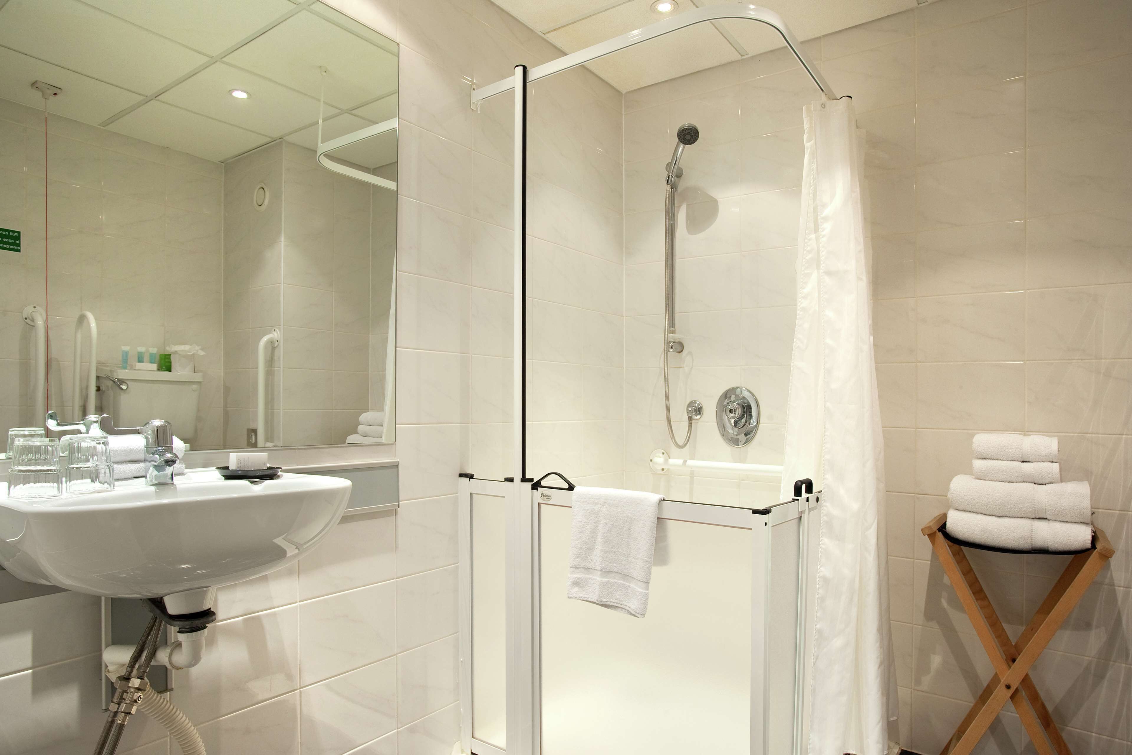 A modern bathroom with a glass-enclosed shower, a sink, and a wooden towel rack.