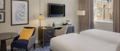 A hotel room with a bed, desk, chair, TV, and artwork on the wall.
