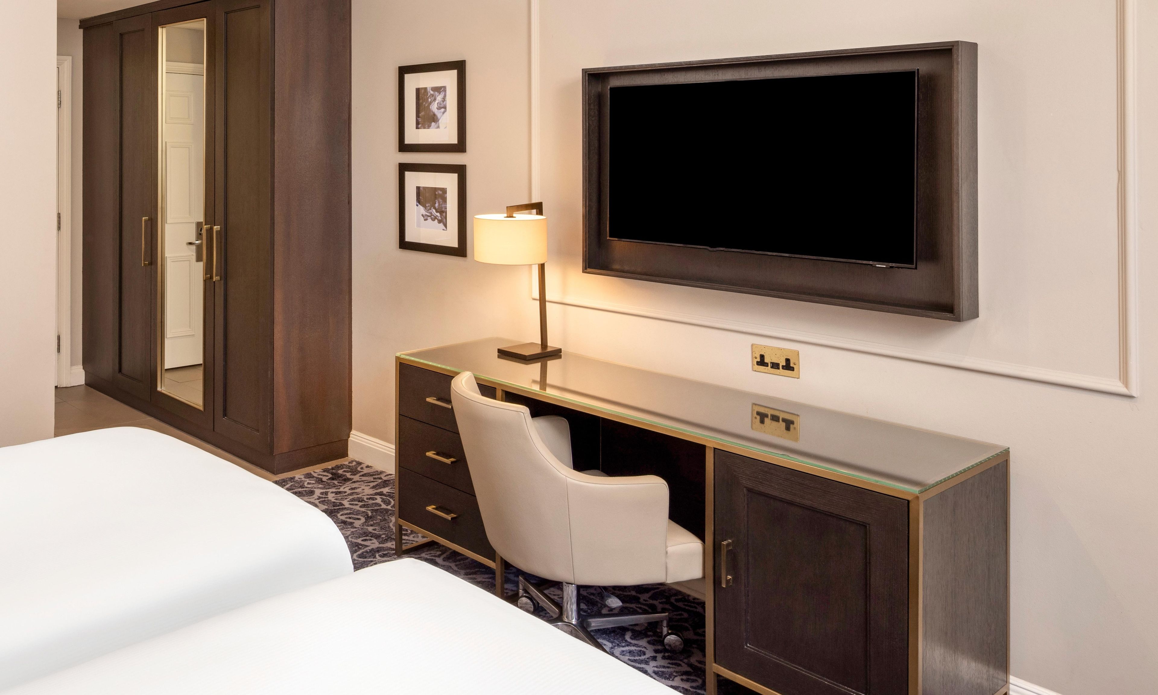 A hotel room with a bed, a desk with a chair, a television, and a wardrobe.