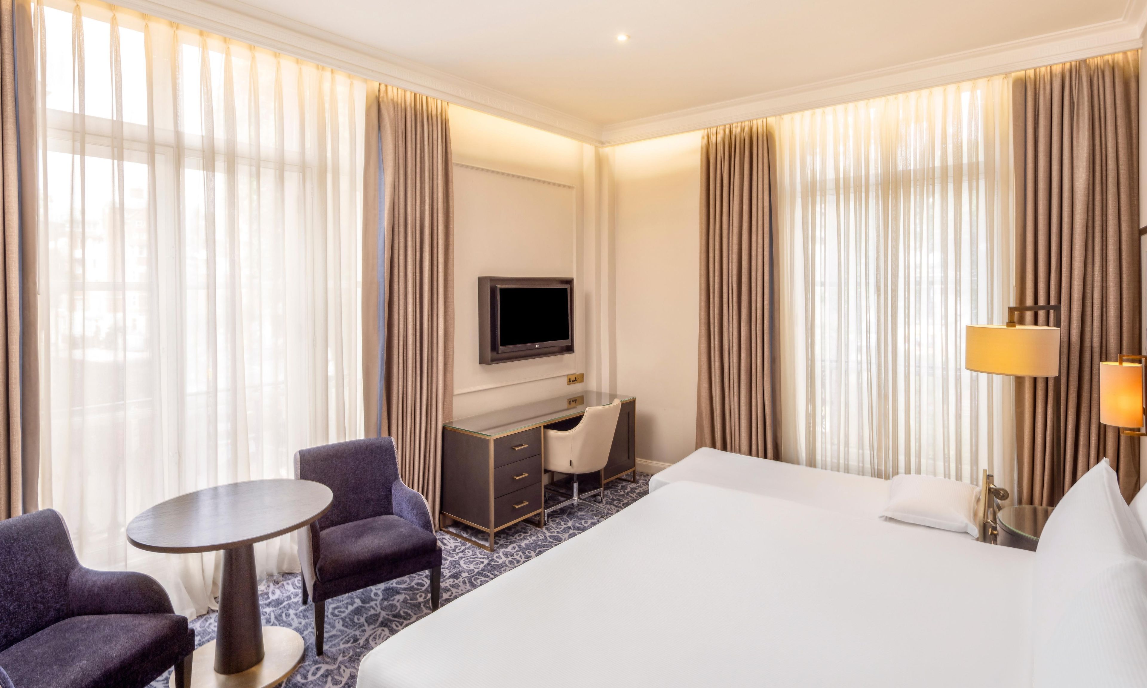 Habitación de hotel con cama, escritorio, silla, televisor y lámpara.