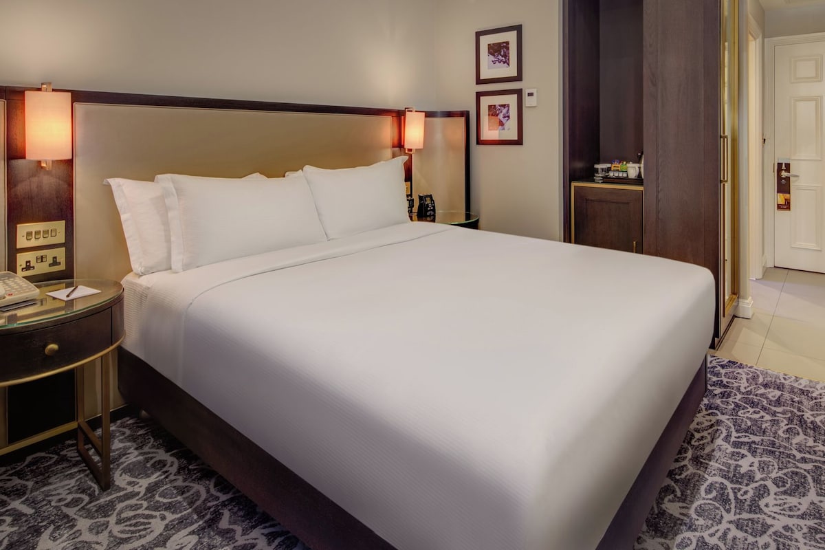 A hotel room with a large bed, bedside lamps, a telephone, and a small table with a lamp.