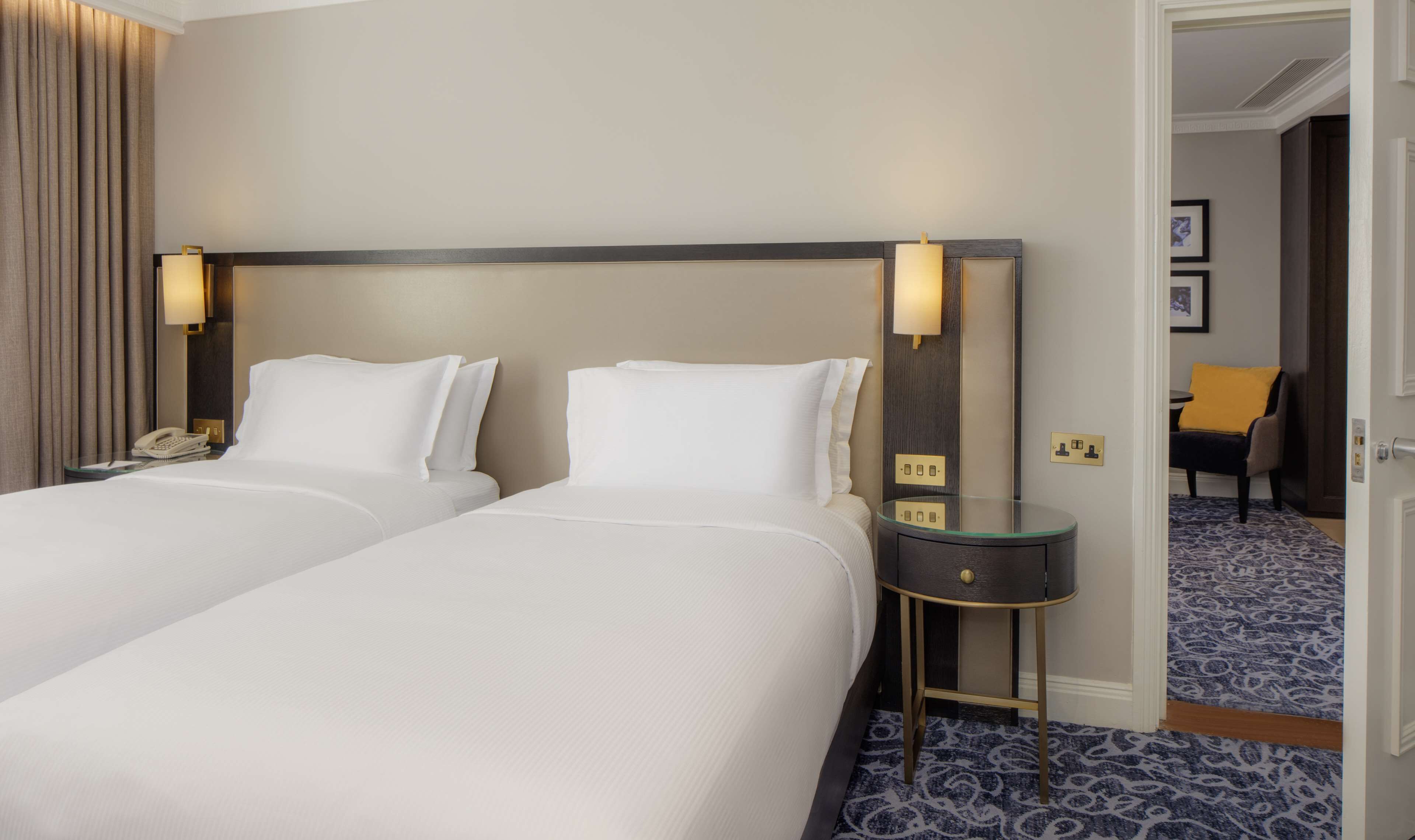 Una habitación de hotel con dos camas, una mesita de noche con teléfono y una pequeña mesa con lámpara.