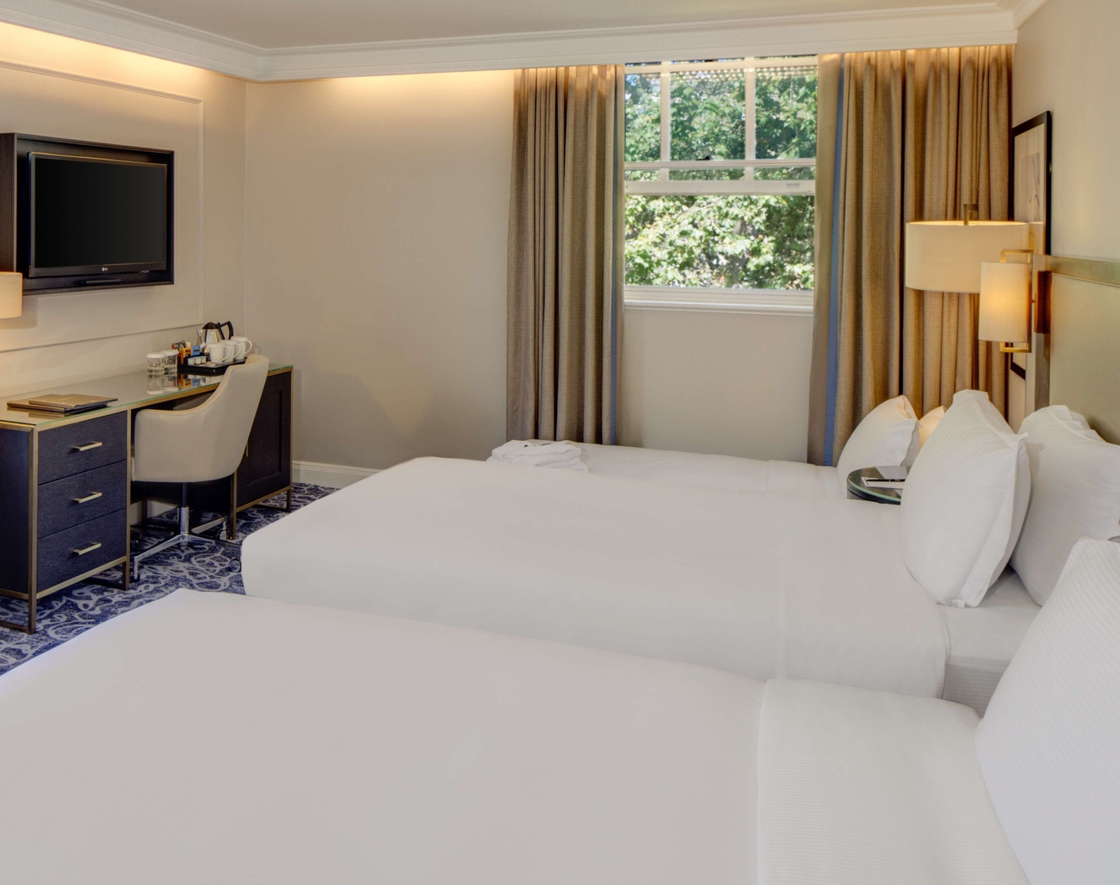 Une chambre d’hôtel avec deux lits, un bureau, une télévision et une fenêtre avec des rideaux.