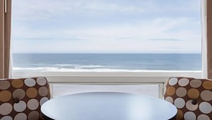 A room with a round table and two chairs with a polka dot pattern, a large window with a view of the ocean. - Seagrass Oceanfront Inn (Newport)