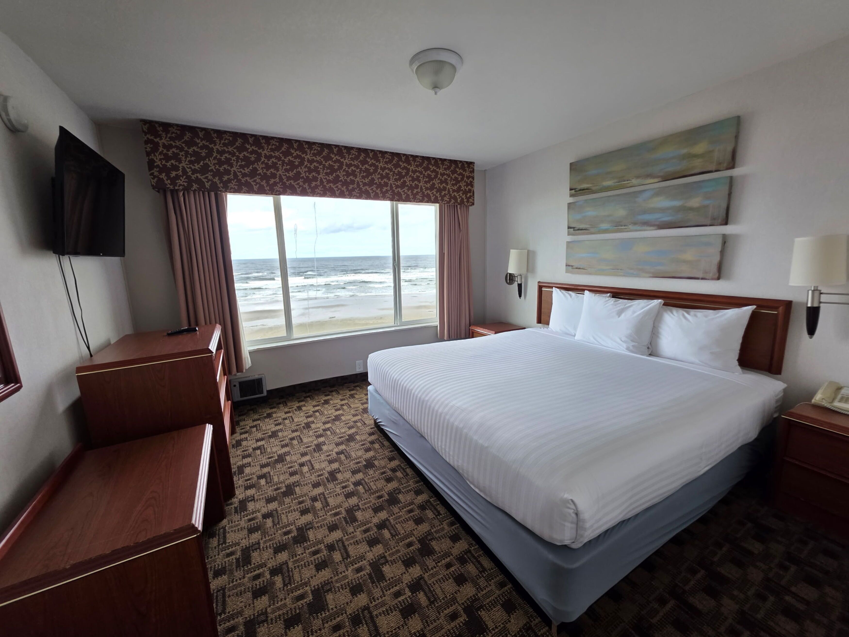 Habitación de hotel con una cama grande, un escritorio, televisión y vista a la playa.