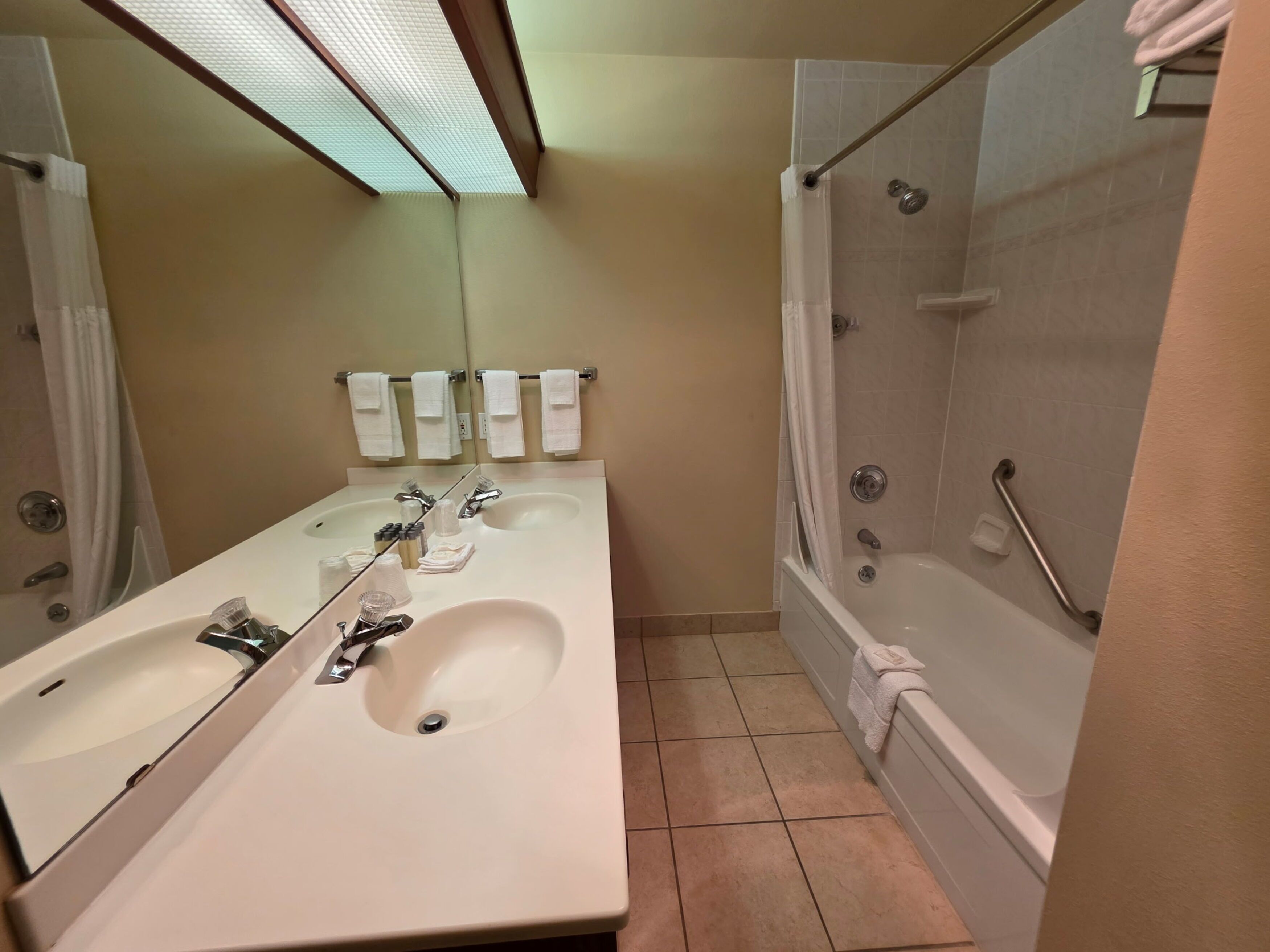 A bathroom with two sinks, a mirror, a shower with a grab bar, and a towel rack.