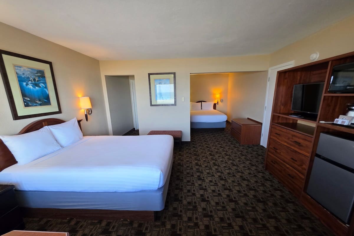 A hotel room with a large bed, a desk, a dresser, a television, and a microwave.