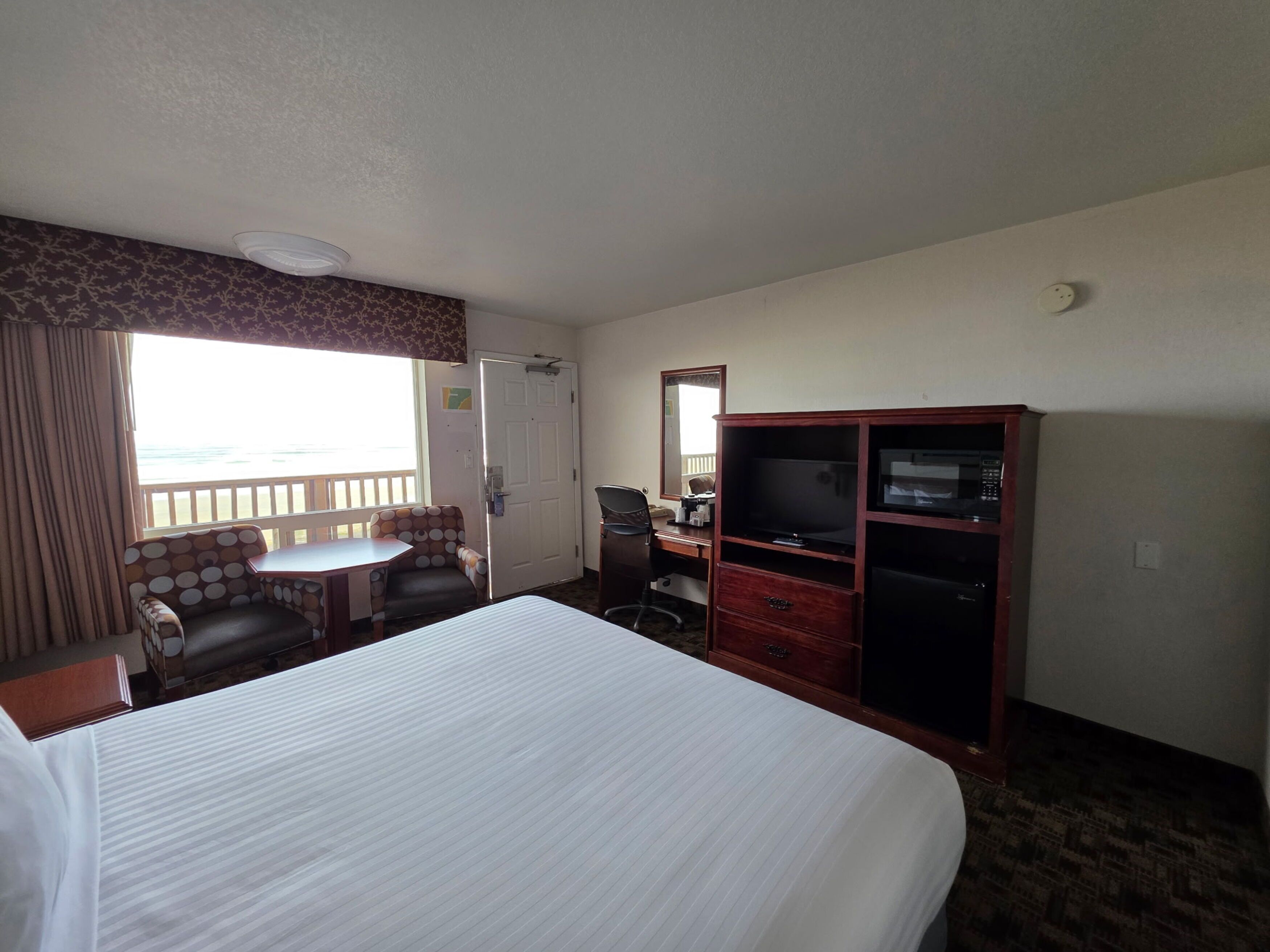 A hotel room with a bed, a desk, a chair, a wardrobe, and a view of the sea.