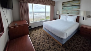 A hotel room with a large bed, a television, a window with a view of the beach, and a painting on the wall. - Seagrass Oceanfront Inn (Newport)