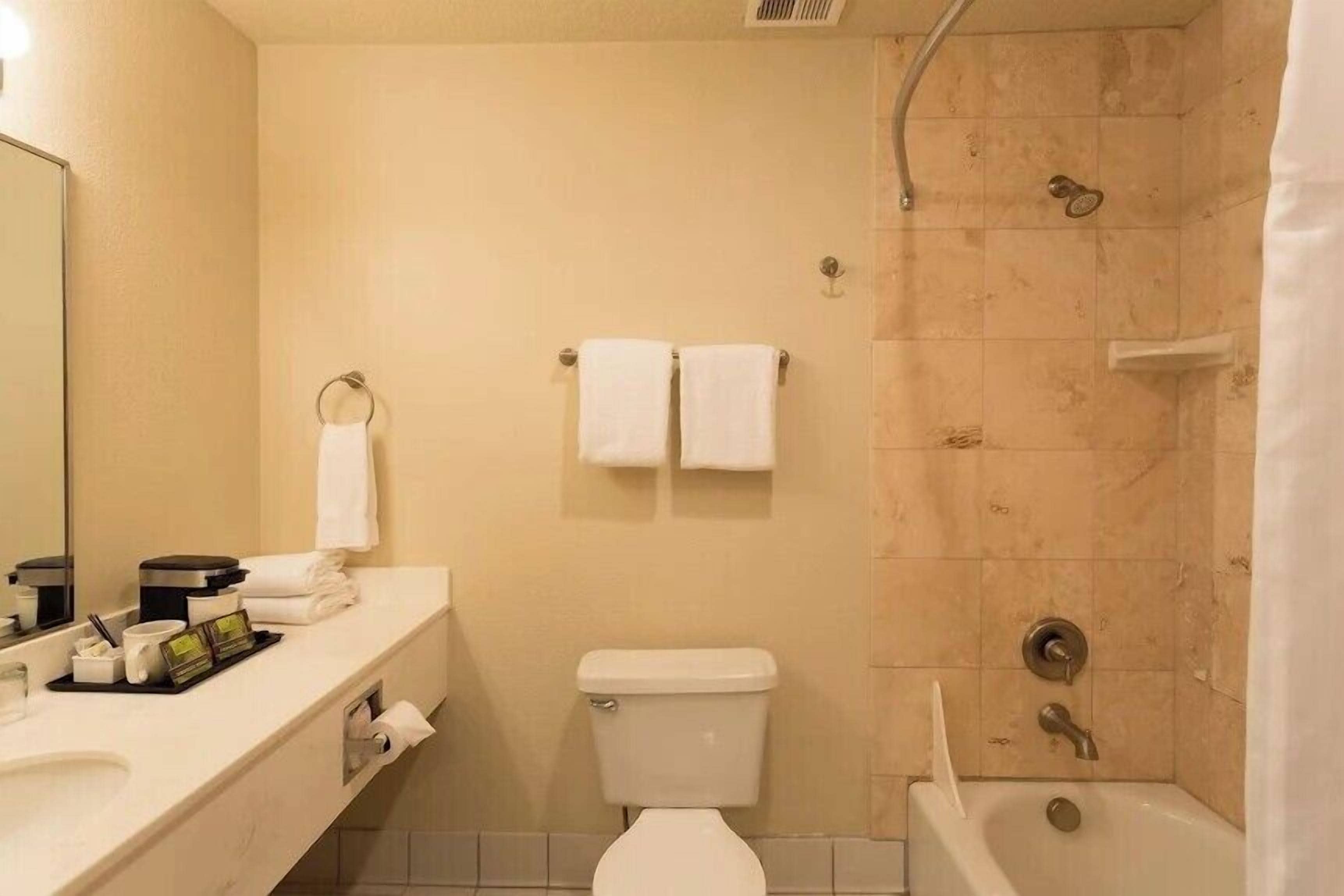 A bathroom with a toilet, sink, and shower. There are towels hanging on hooks.