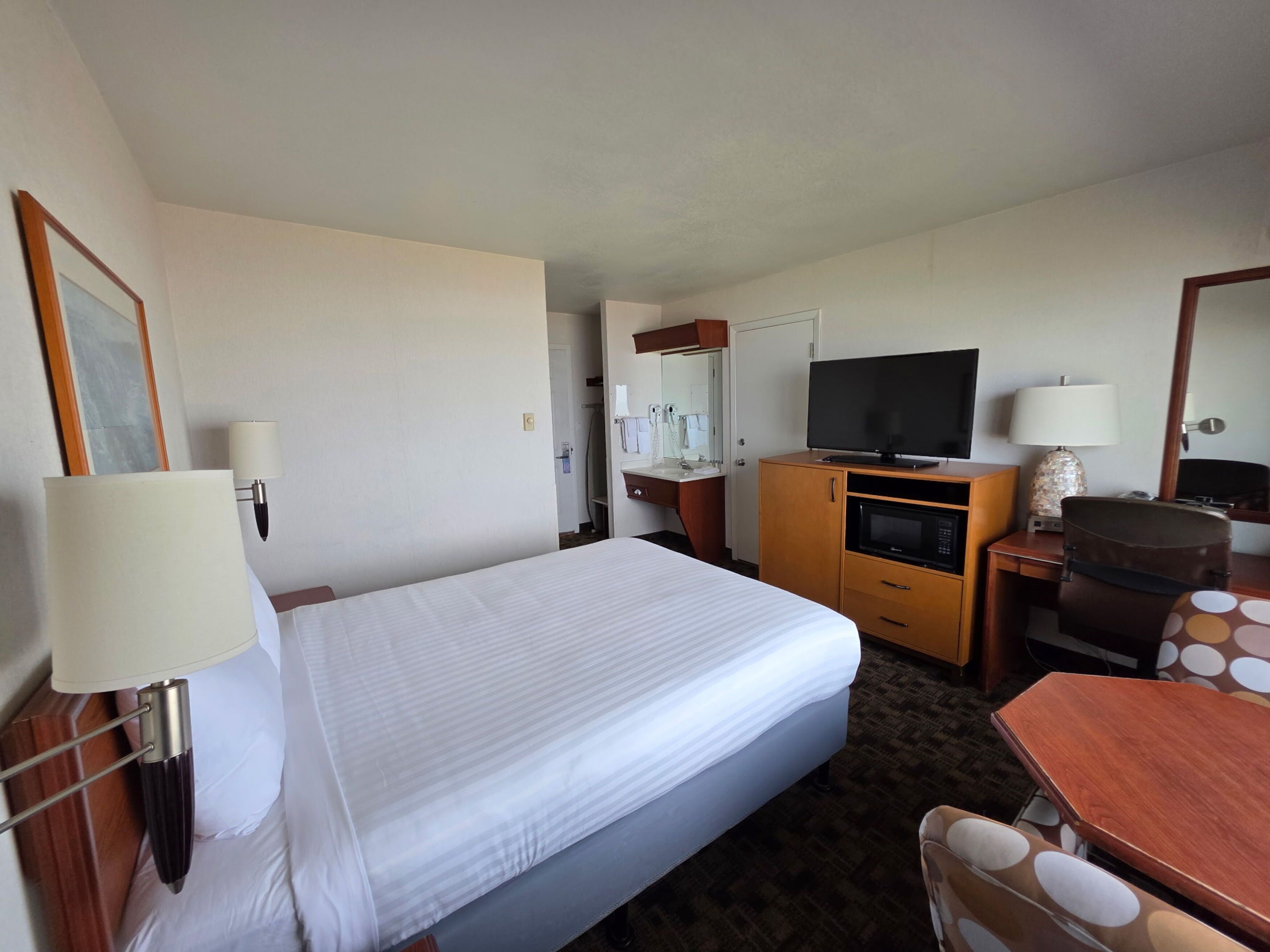 A hotel room with a bed, a television, a desk, a chair, and a bathroom visible through an open door.