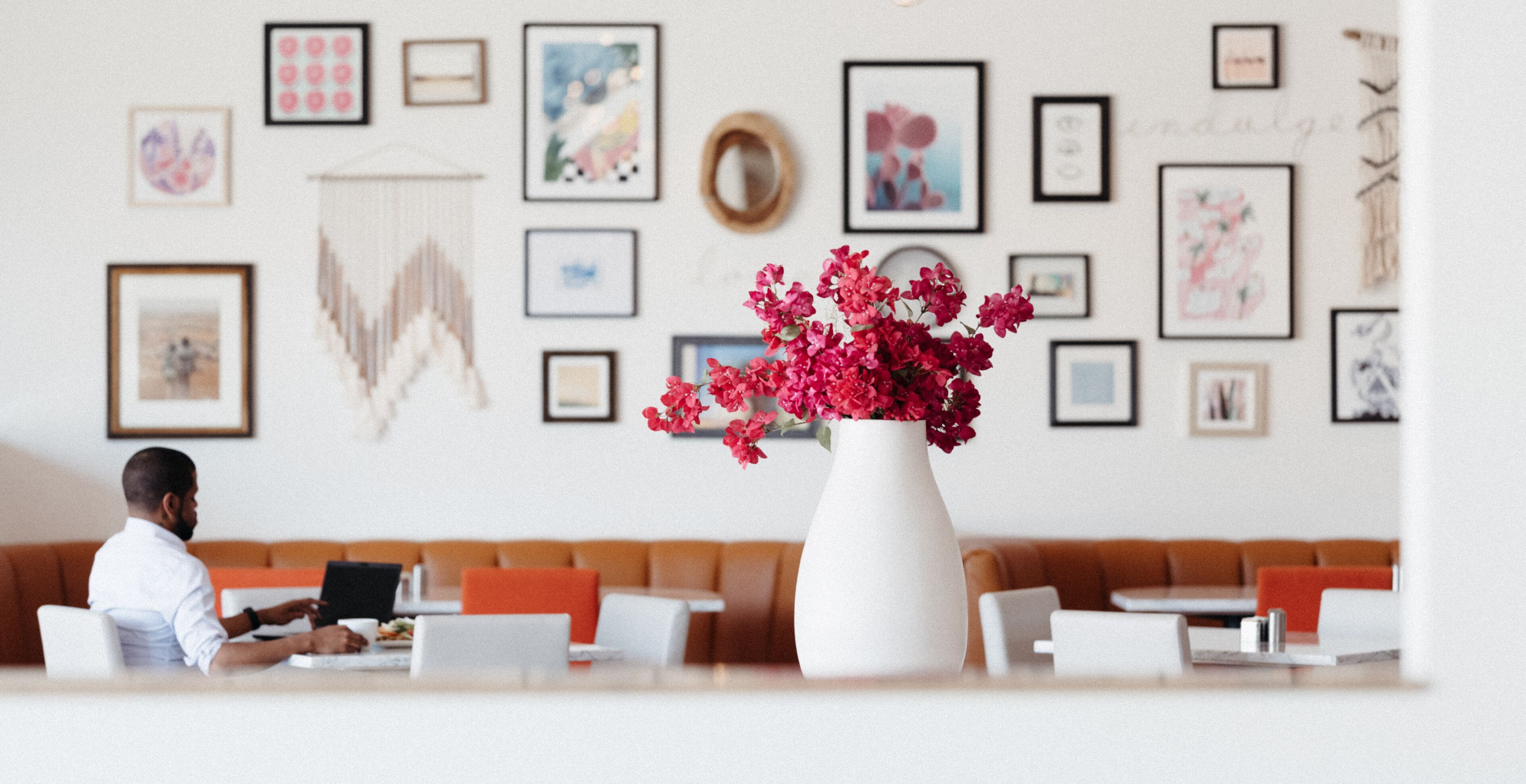 A modern hotel lobby with a seating area, a large white vase with red flowers, and various framed artworks on the walls.