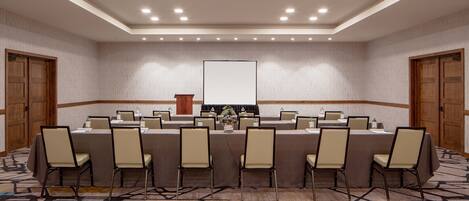 Un salón de conferencias con una larga mesa, sillas, un atril y una pantalla.