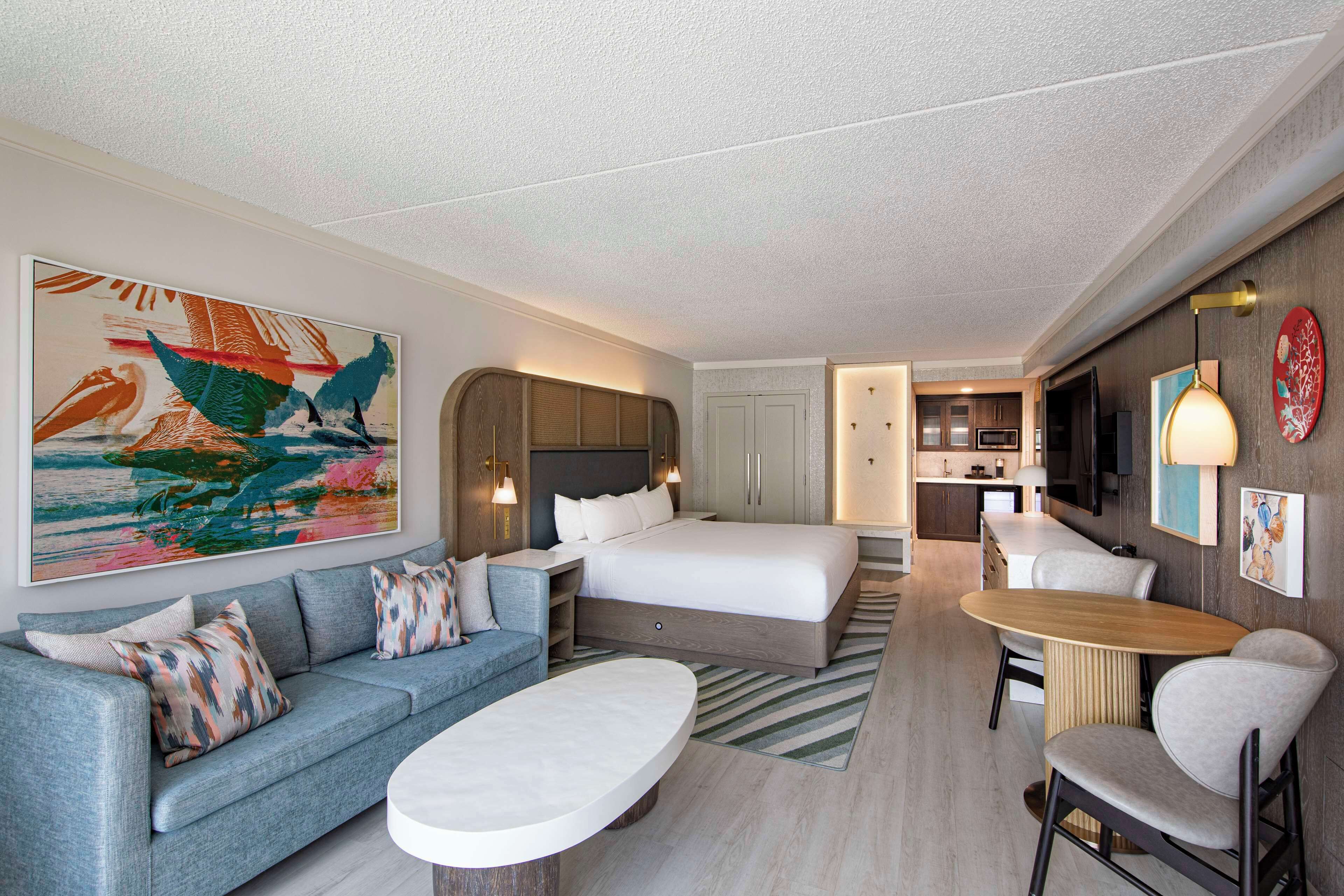A hotel room with a bed, a sofa, a coffee table, a TV, and a kitchen area.