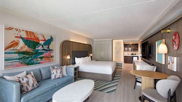 Una habitación de hotel con cama, sofá, mesa de centro, televisor y zona de cocina.
