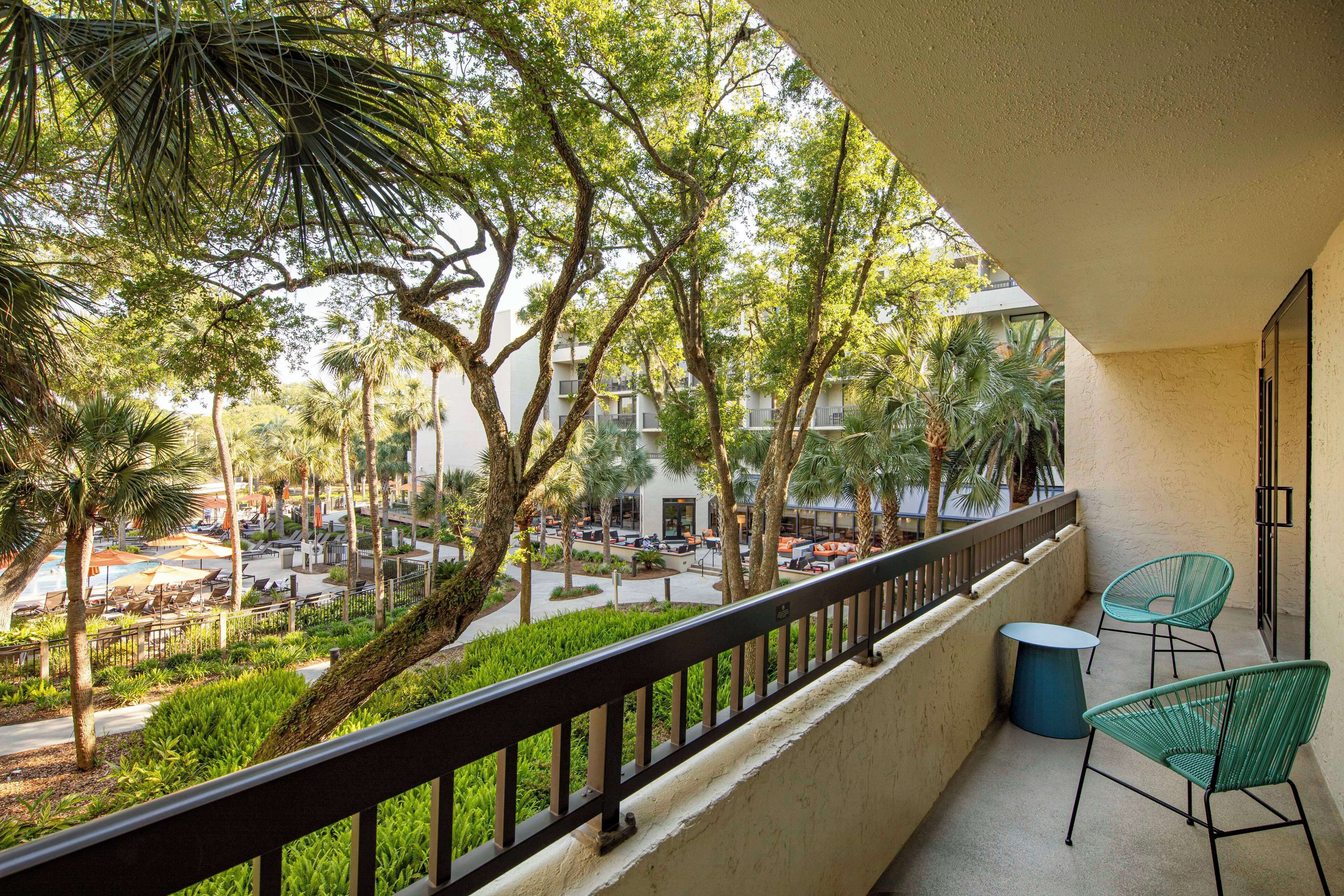 A balcony with a view of a courtyard, including outdoor seating and palm trees.
