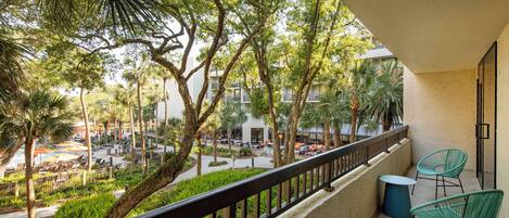 A balcony with a view of a courtyard, including outdoor seating and palm trees.
