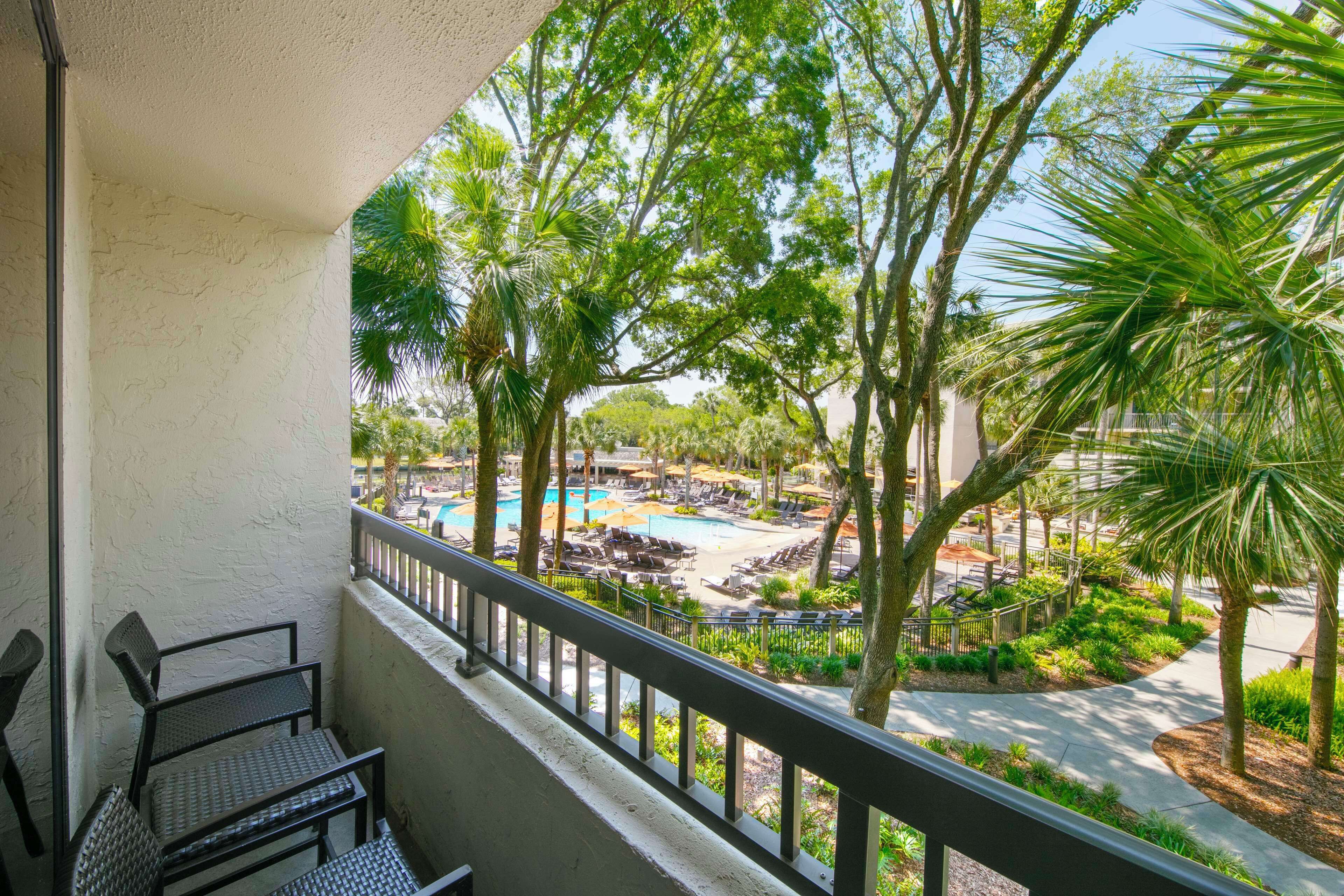 A balcony with a view of a pool area, surrounded by palm trees and lounge chairs.