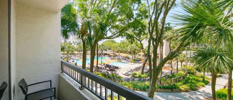 A balcony with a view of a pool area, surrounded by palm trees and lounge chairs.