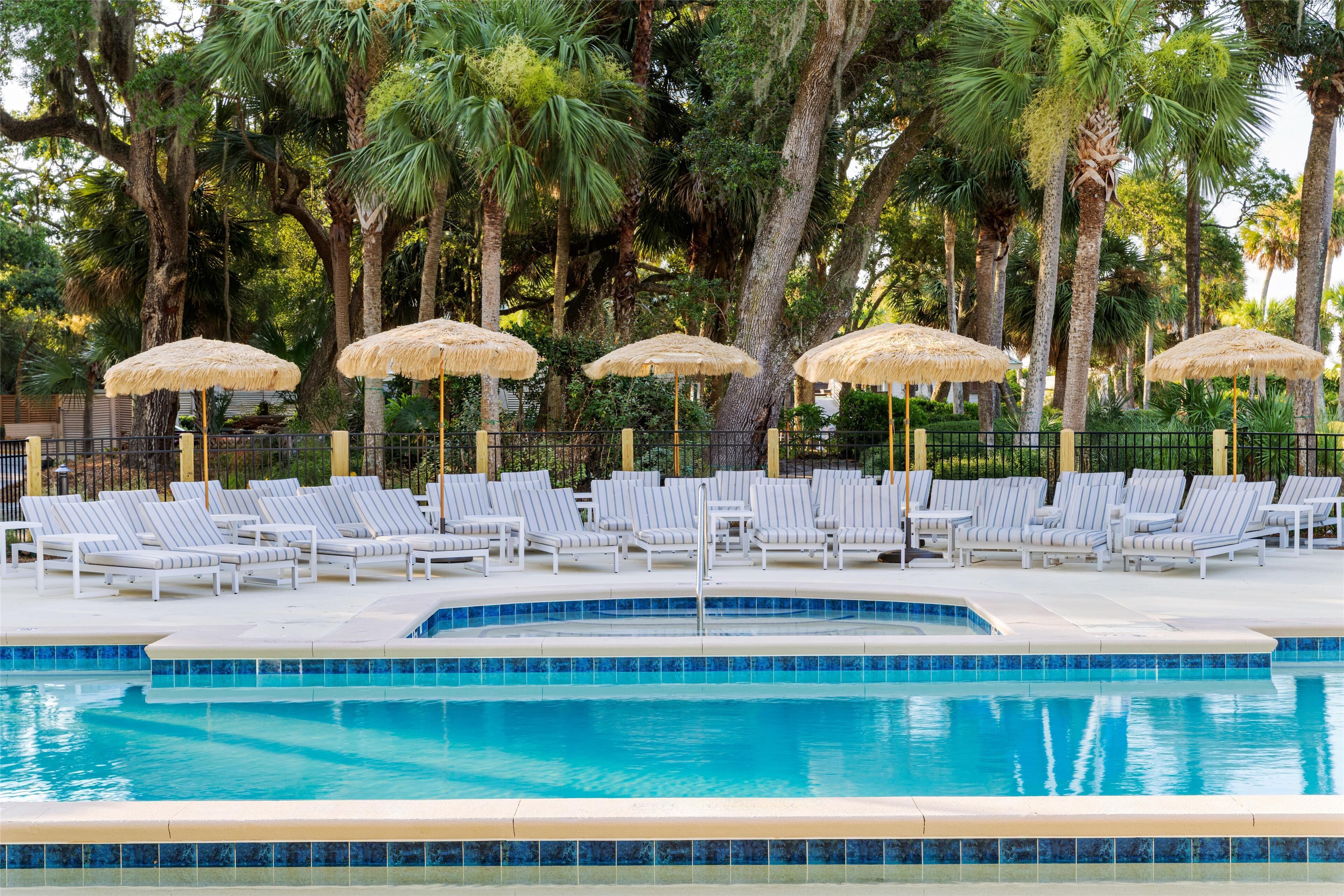 A pool area with lounge chairs and thatched umbrellas, surrounded by palm trees.