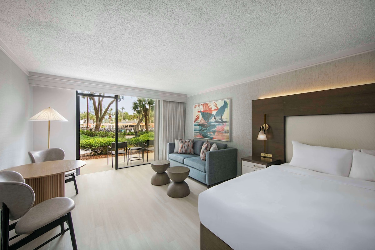 Una habitación de hotel moderna con una cama grande, un sofá, una mesa de comedor y vistas al exterior.