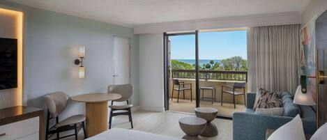 Quarto de hotel com cama, escrivaninha, cadeira, mesa pequena, sofá e varanda com vista para o mar.