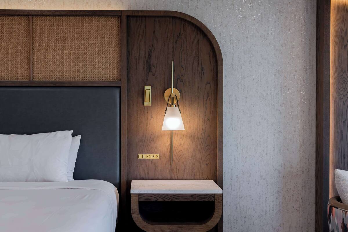 Ein ordentlich bezogenes Bett mit weißen Leinen, einem Holz-Kopfteil und einem an der Wand befestigten Nachttisch mit Lampe.