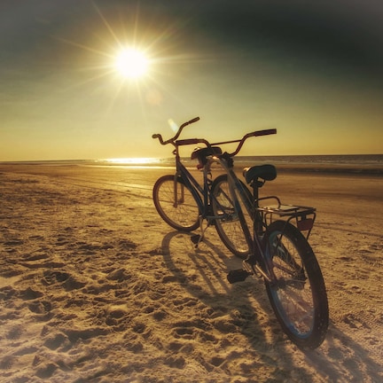 A bicycle parked on a sandy beach with the sun low on the horizon.