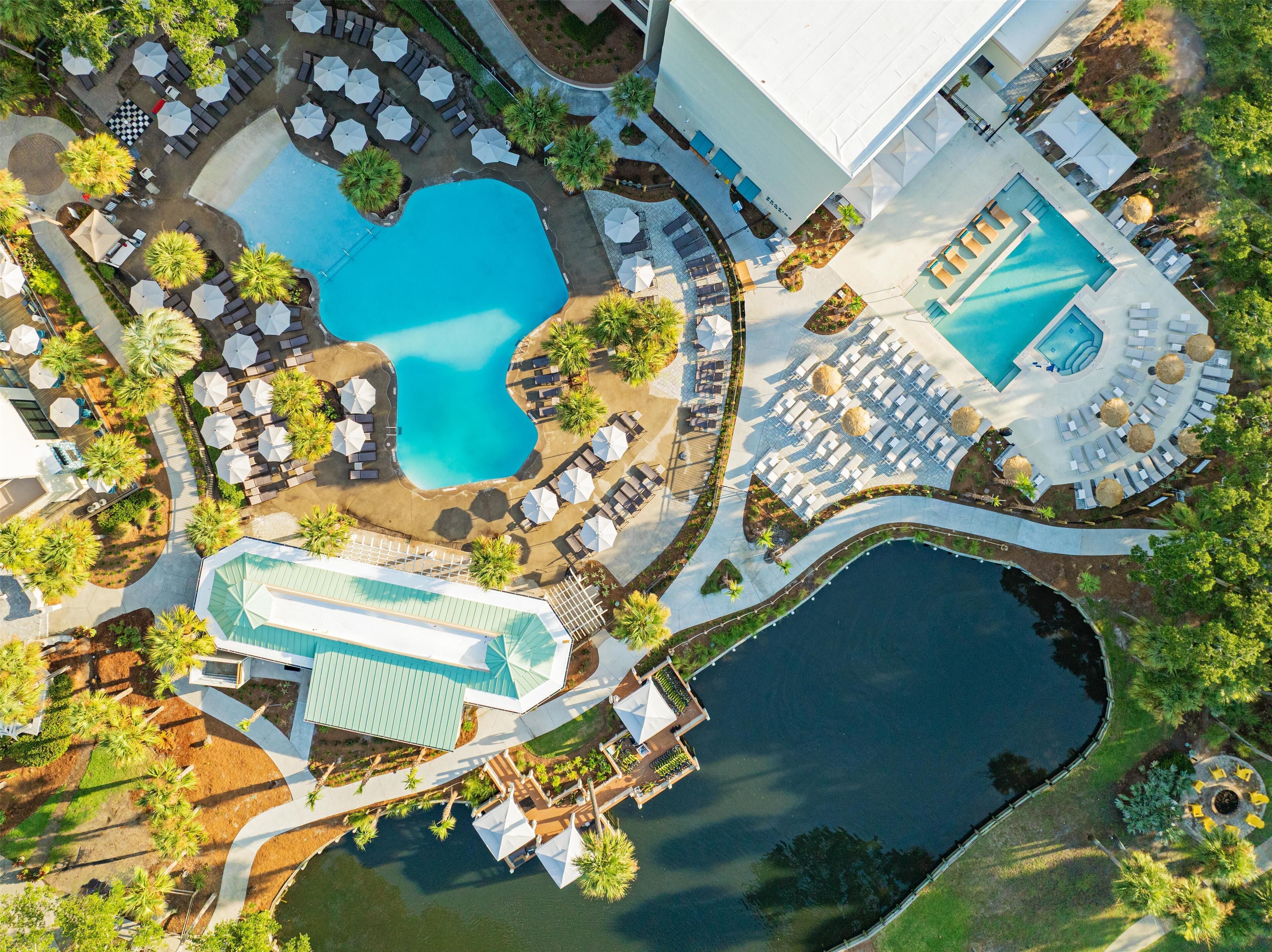 Une vue aérienne d’un complexe hôtelier doté de plusieurs piscines, de chaises longues et d’un grand bâtiment surmonté d’un toit végétalisé.