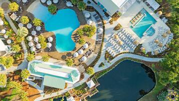 Une vue aérienne d’un complexe hôtelier doté de plusieurs piscines, de chaises longues et d’un grand bâtiment surmonté d’un toit végétalisé.