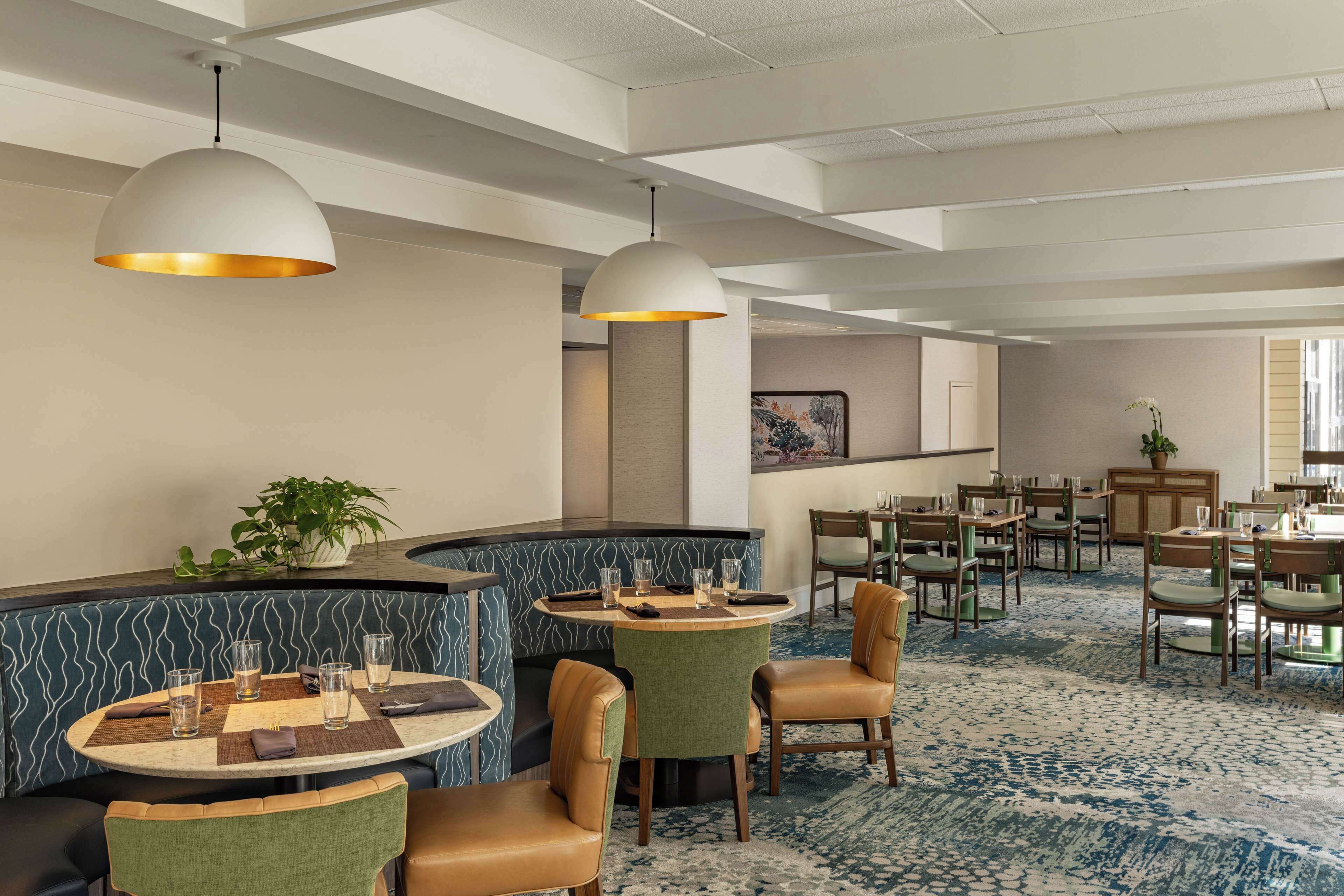 A hotel lobby with round tables, green upholstered chairs, and pendant lighting.