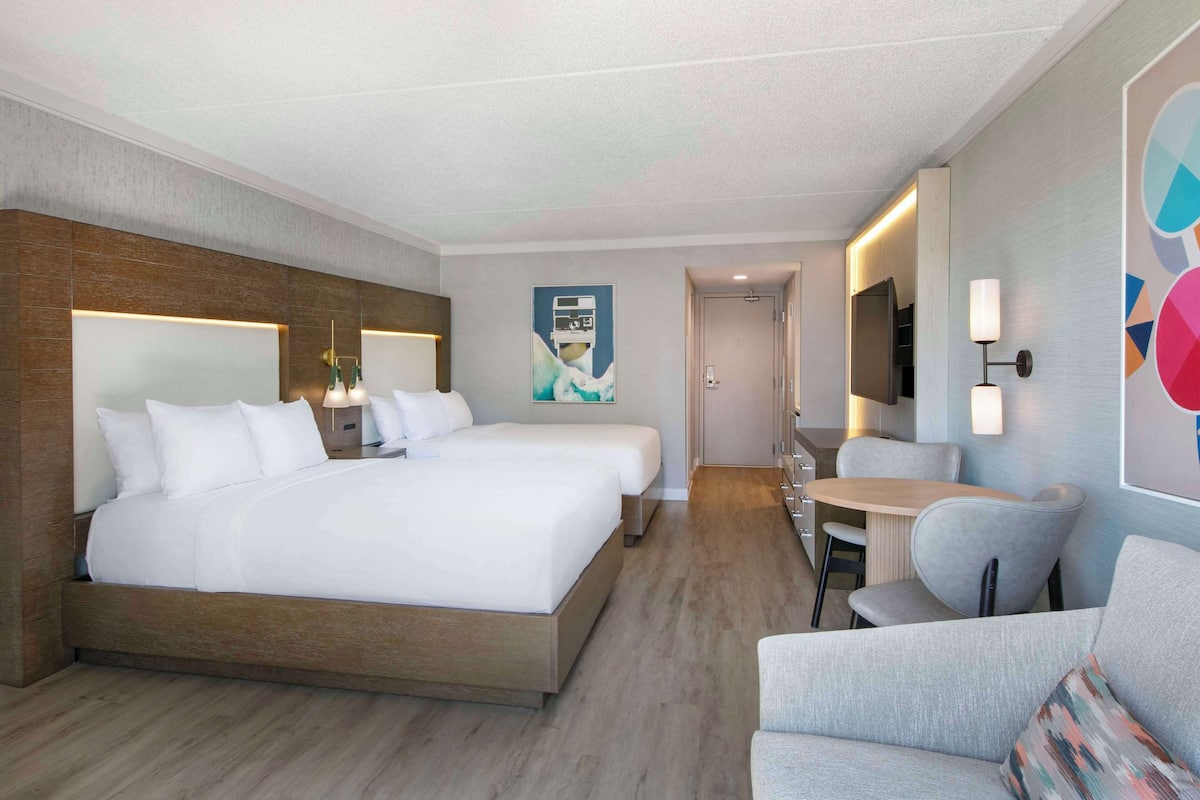 Habitación de hotel con una cama grande, un escritorio y una silla. Hay un televisor en la pared y un cuadro también en la pared.
