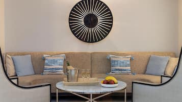 Una sala de estar moderna con un sofá color beige, dos almohadones estampados, una mesa de centro redonda con un cuenco de frutas y un adorno en la pared.