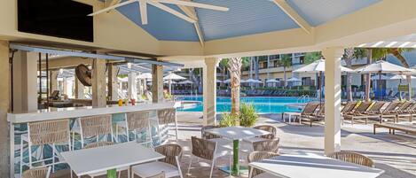 A covered outdoor area with tables and chairs, a pool, and umbrellas.