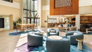 Een ruime lobby met een hoge plafond, een centraal zithoek met banken en stoelen, een eetgedeelte met tafels en stoelen, en een bar met flessenkasten.