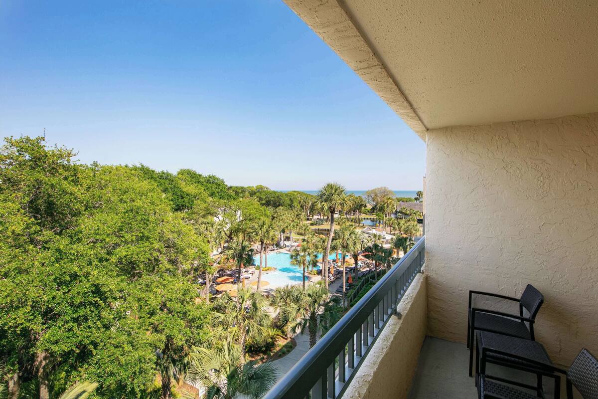 Un balcón con vista a una piscina de resort rodeada de palmeras y vegetación.