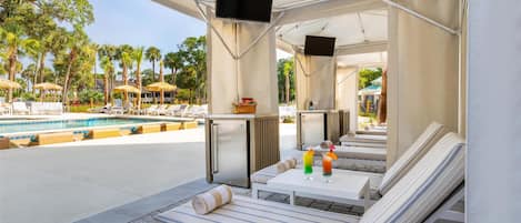 A poolside lounge area with sun loungers, a small table with drinks, and a TV screen.