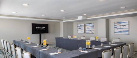 Un salón de conferencias con una mesa larga, sillas, una pantalla de televisión y obras de arte en las paredes.