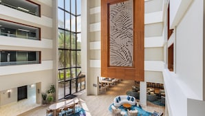 Een moderne hotel lobby met een centraal zitgedeelte, meerdere verdiepingen en grote ramen.