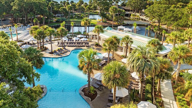 Een resort met een groot zwembad, palmbomen en uitzicht op de oceaan.