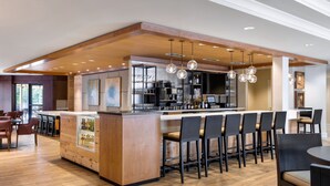 A modern bar area with a wooden bar counter, multiple bar stools, and pendant lighting.