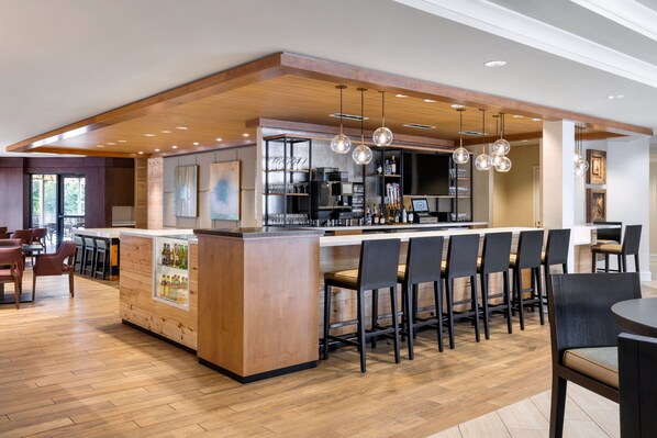 A modern bar area with a wooden bar counter, multiple bar stools, and pendant lighting. - Sheraton by Marriott Atlanta Perimeter Dunwoody (Atlanta)