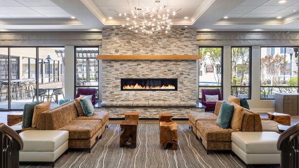 A modern lounge area with a stone fireplace, comfortable seating, and large windows offering views of the outdoors.