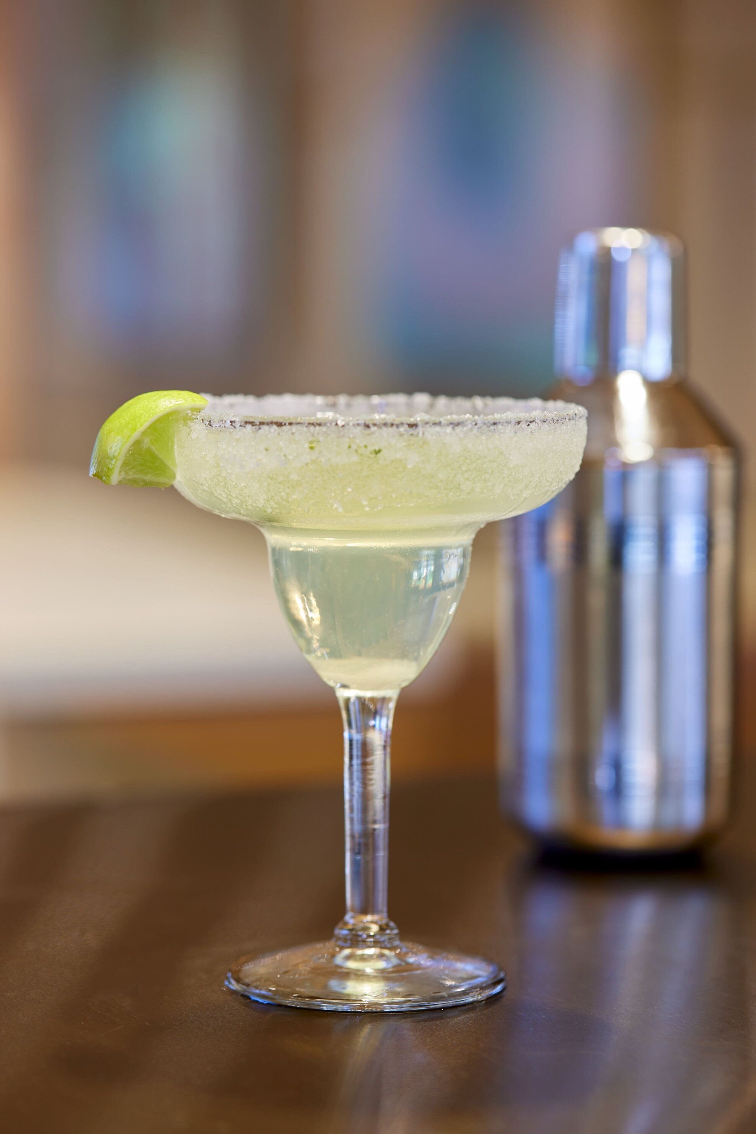 A margarita glass with a lime garnish on a wooden table.