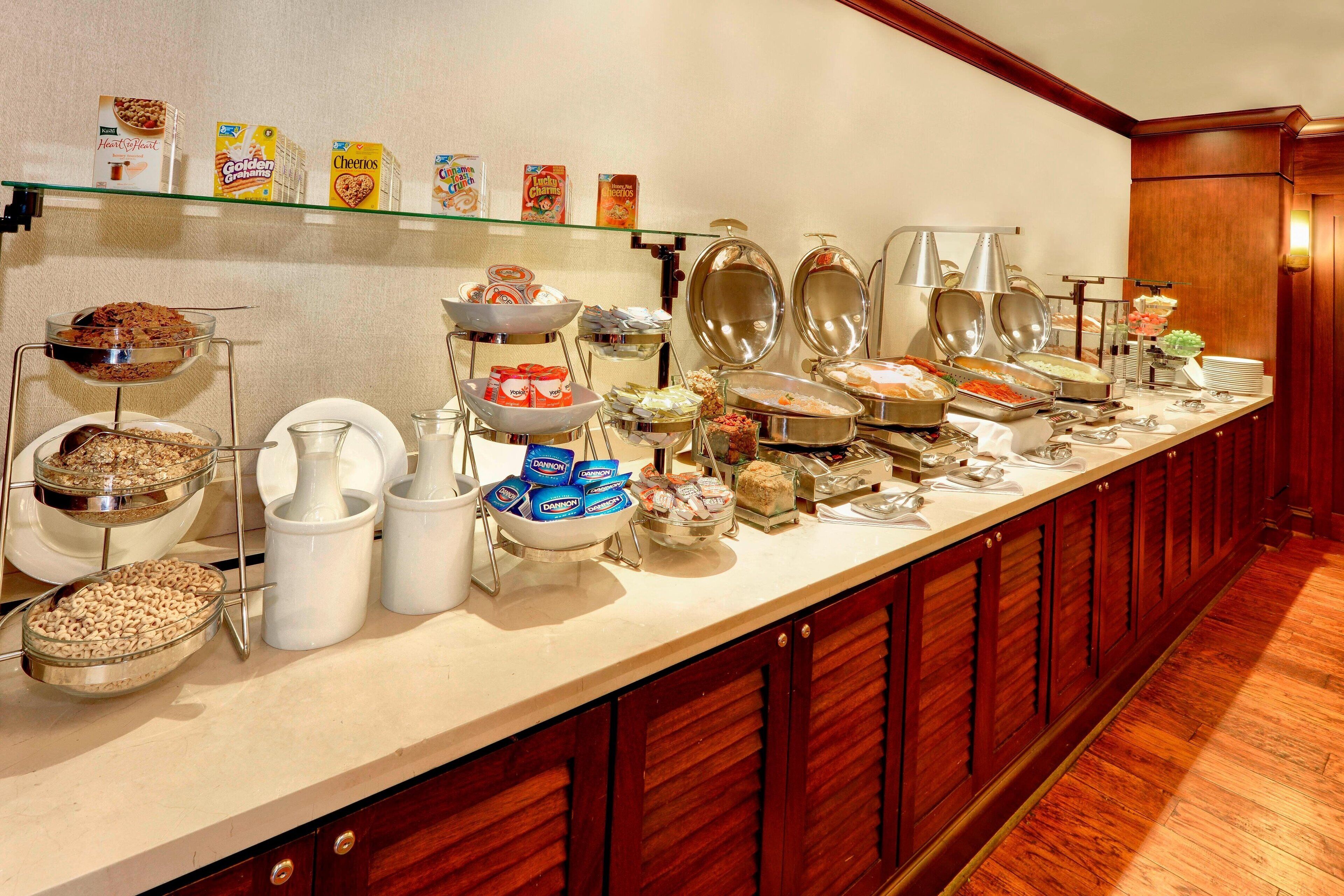 A buffet with various food items and containers, including cereals, fruits, and desserts.