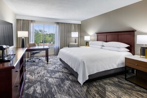 A hotel room with a large bed, a desk with a chair, a TV, and a window with curtains.