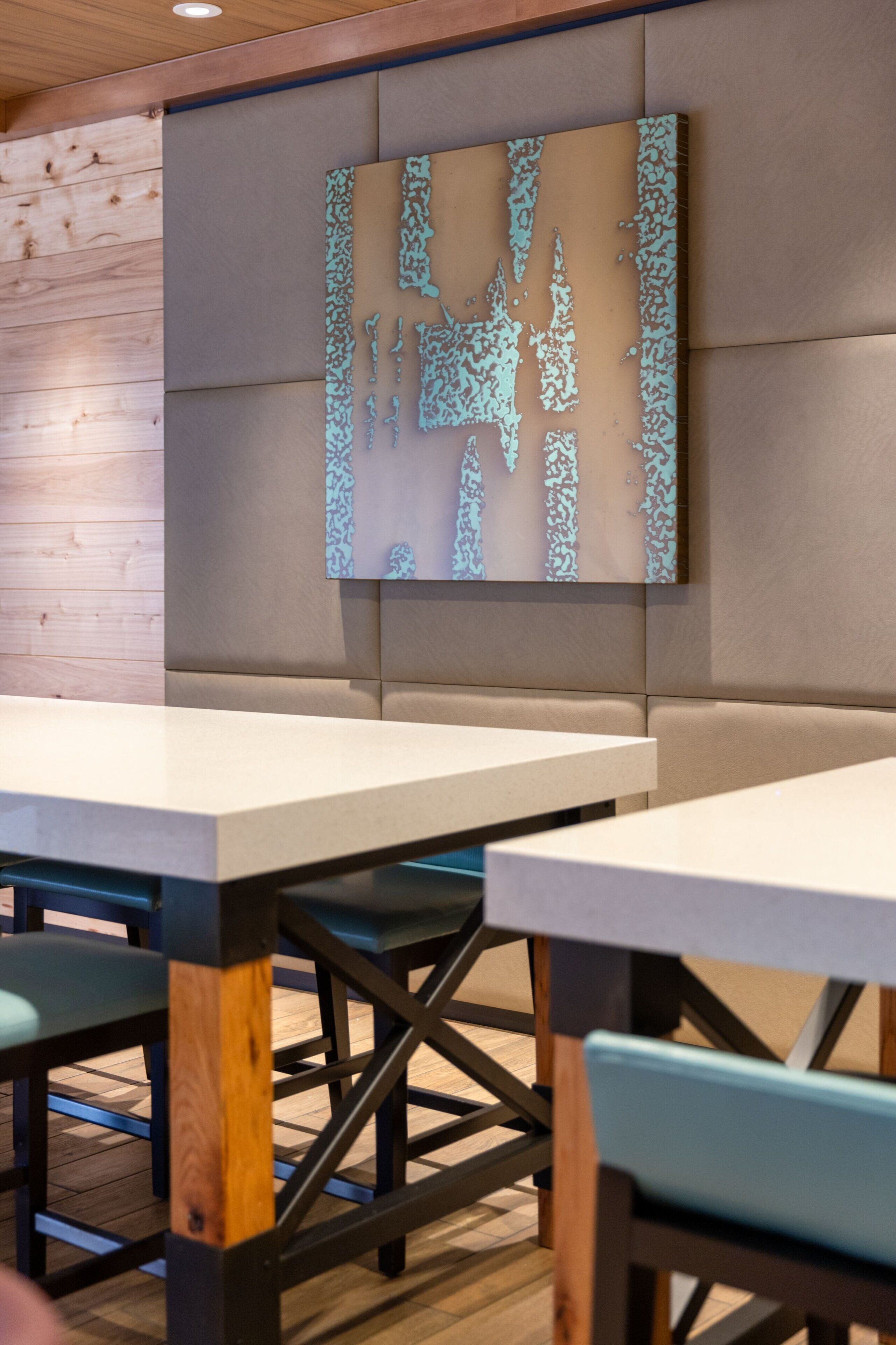 Un intérieur de restaurant moderne avec des murs lambrés en bois, des tables blanches et des chaises de couleur turquoise.