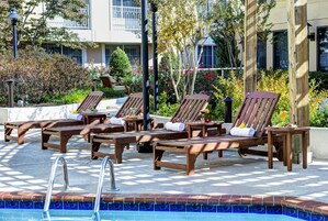 A poolside area with wooden lounge chairs, a pool, and a garden with various plants and flowers.