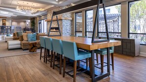 A modern dining area with a wooden table and blue chairs, a stone fireplace, and large windows offering a view of the outdoors.