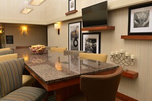 A conference room with a granite table, cushioned chairs, a fruit bowl, framed pictures, and a flat-screen TV.